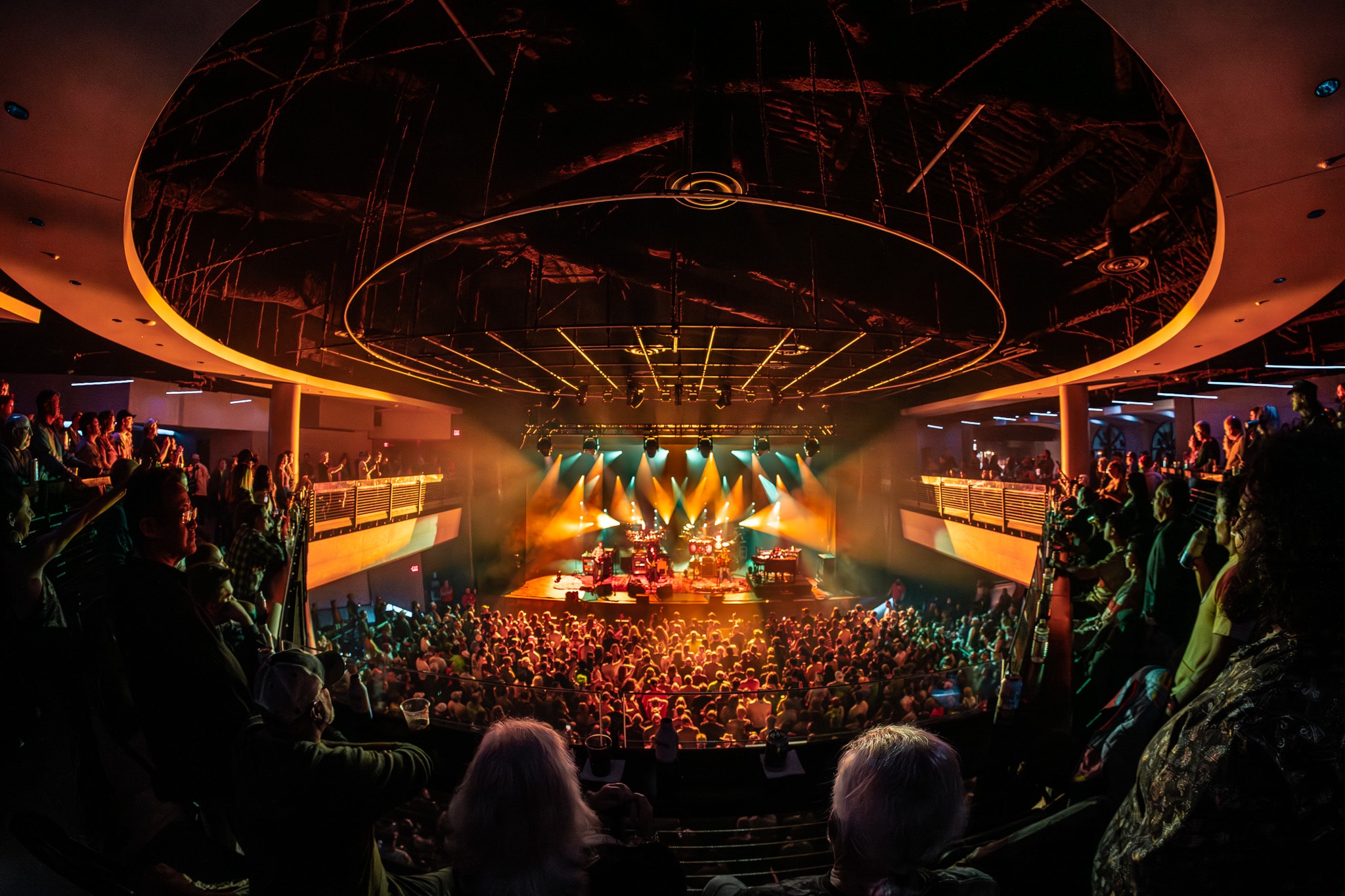 Concert hall wide shot with warm orange stage lighting and crowd