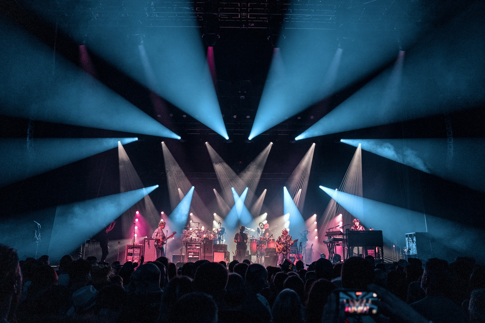 Full band on stage with dramatic blue and pink light beams