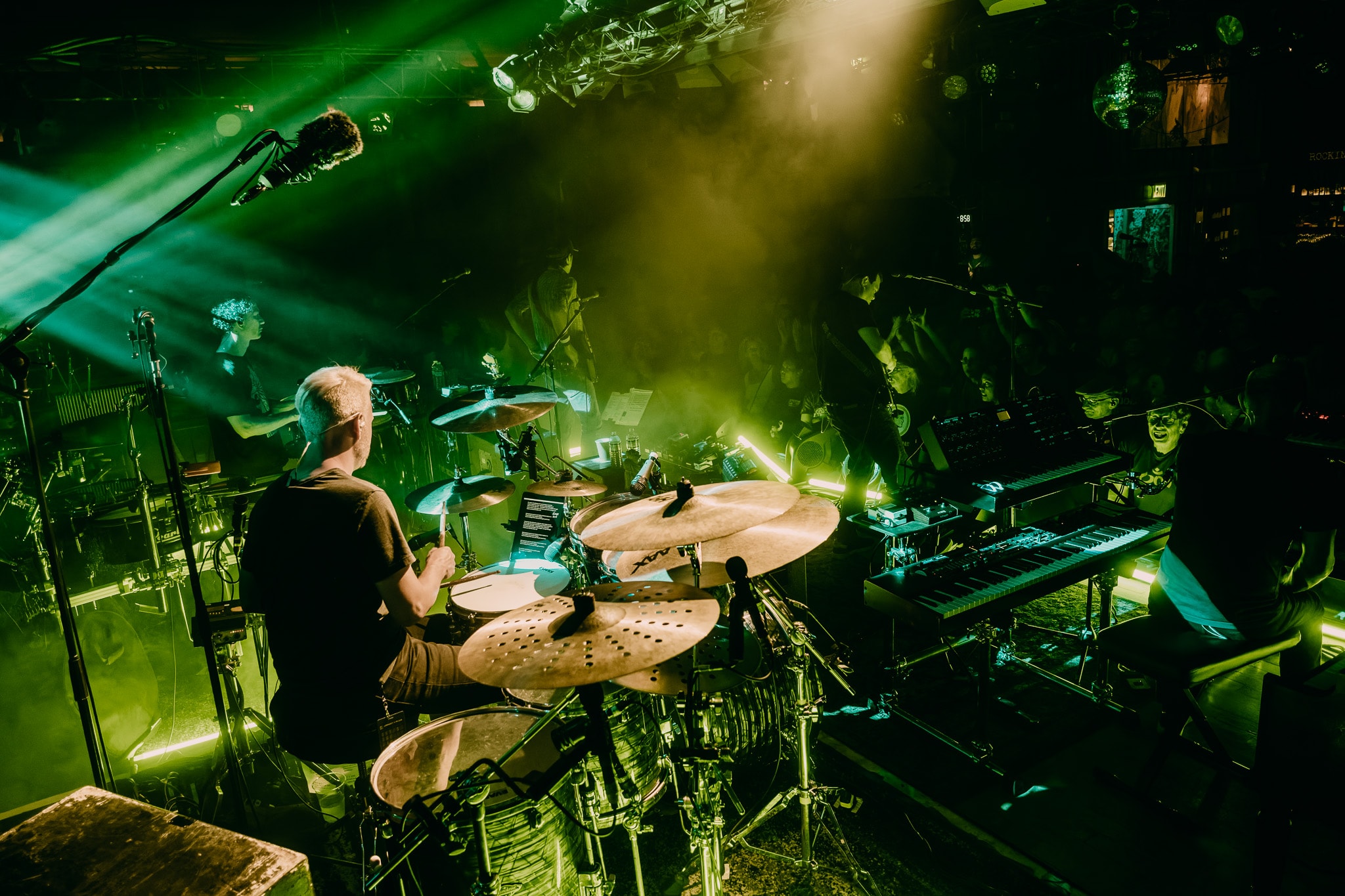 Drummer and keyboardist with green stage lighting and crowd