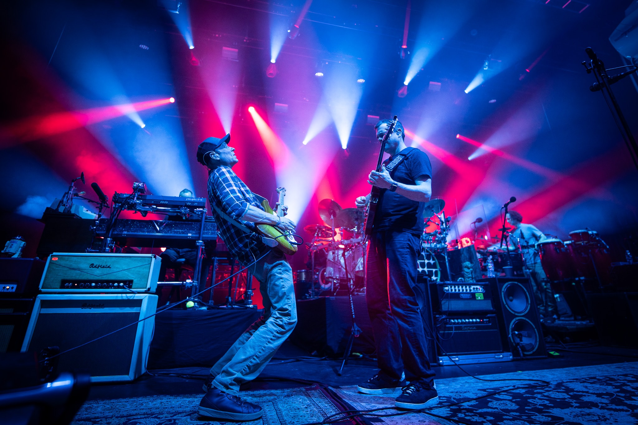 Two guitarists performing on stage with blue and red light beams