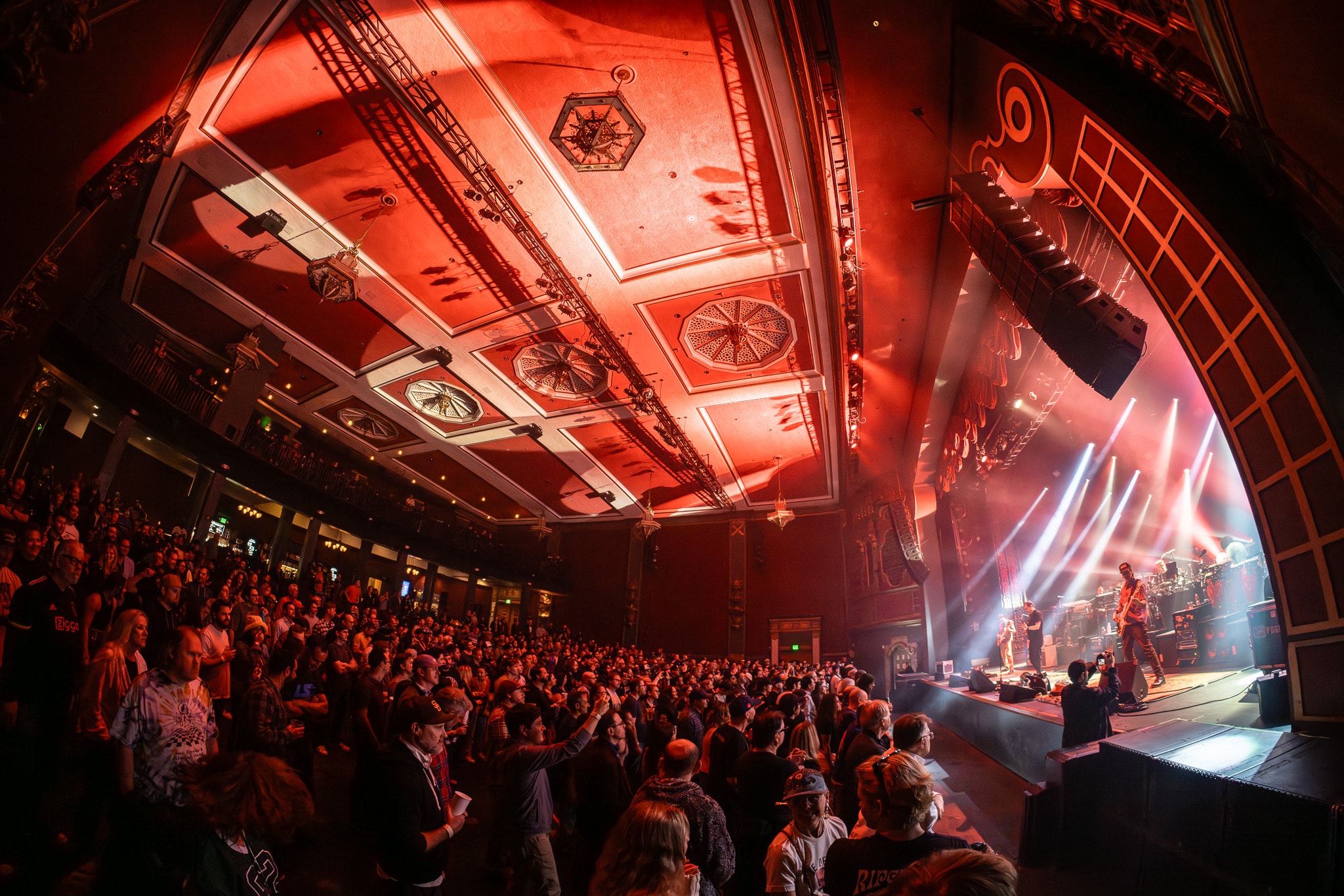 Wide angle view of packed concert hall with red lighting and stage